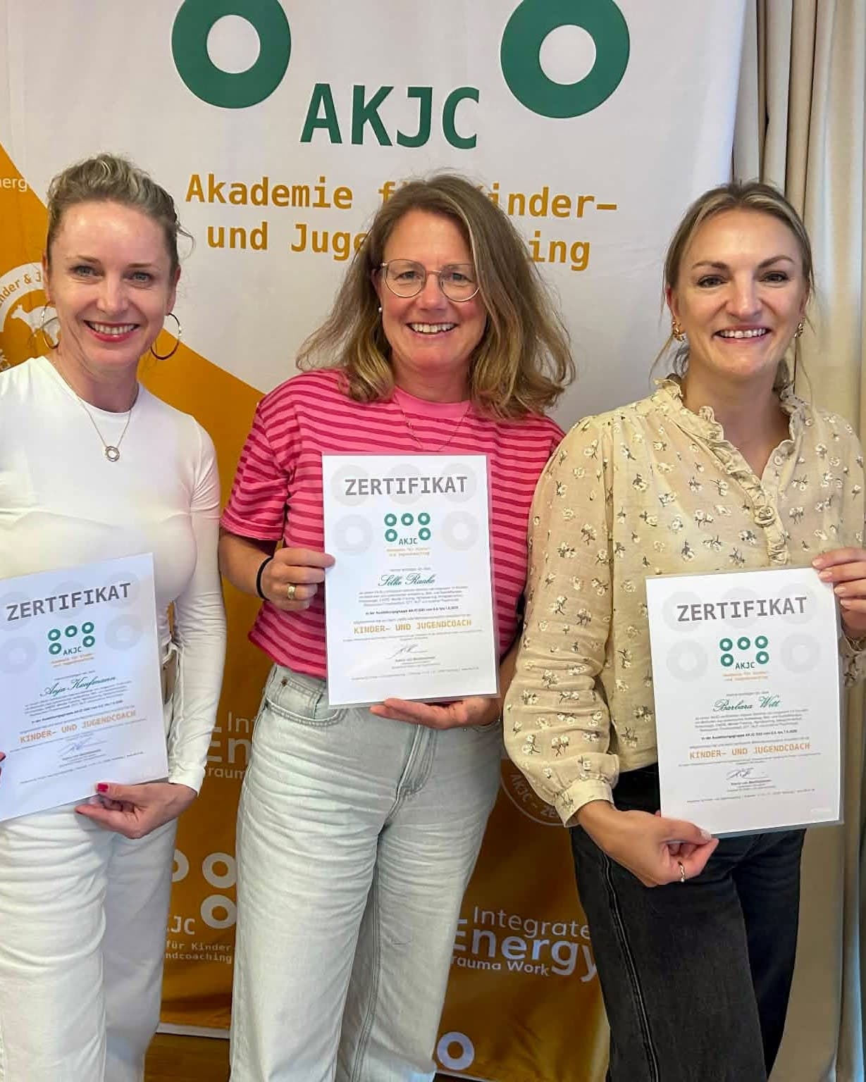 Absolventinnen halten ihre Zertifikate «Kinder- und Jugendcoach» vor dem AKJC-Banner